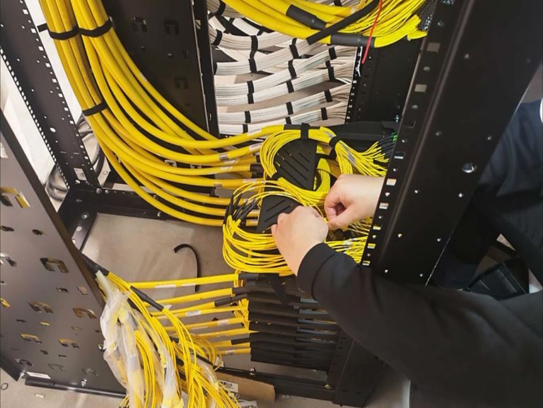 Technician dressing yellow fibre cables in an equipment rack