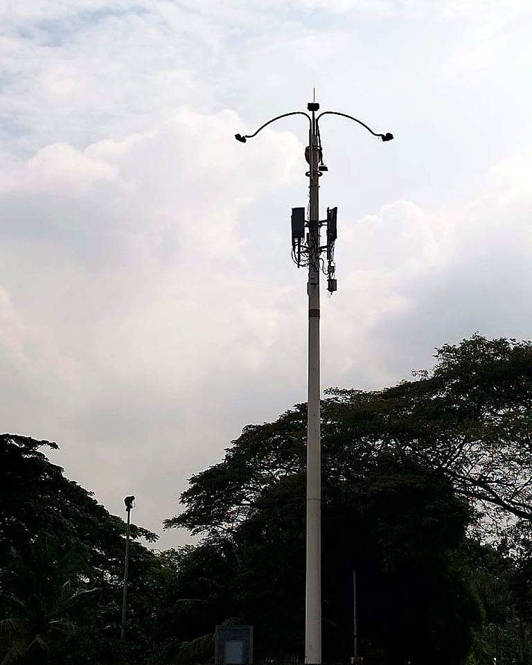Lamp pole carrying cellular antennas, silhouetted against clouds