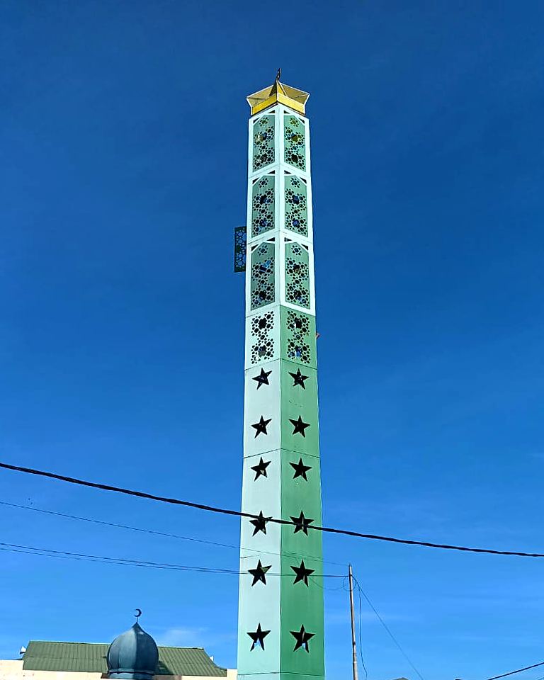 Green and white minaret-style monopole beside a surau
